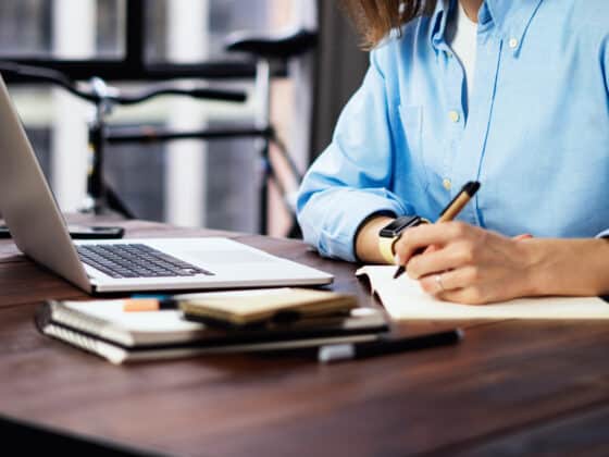 Young female content marketer wearing a blue button up shirt works with a laptop and notepad.