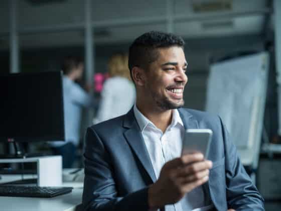 Executive using mobile phone in office, wearing a grey suit and white shirt.